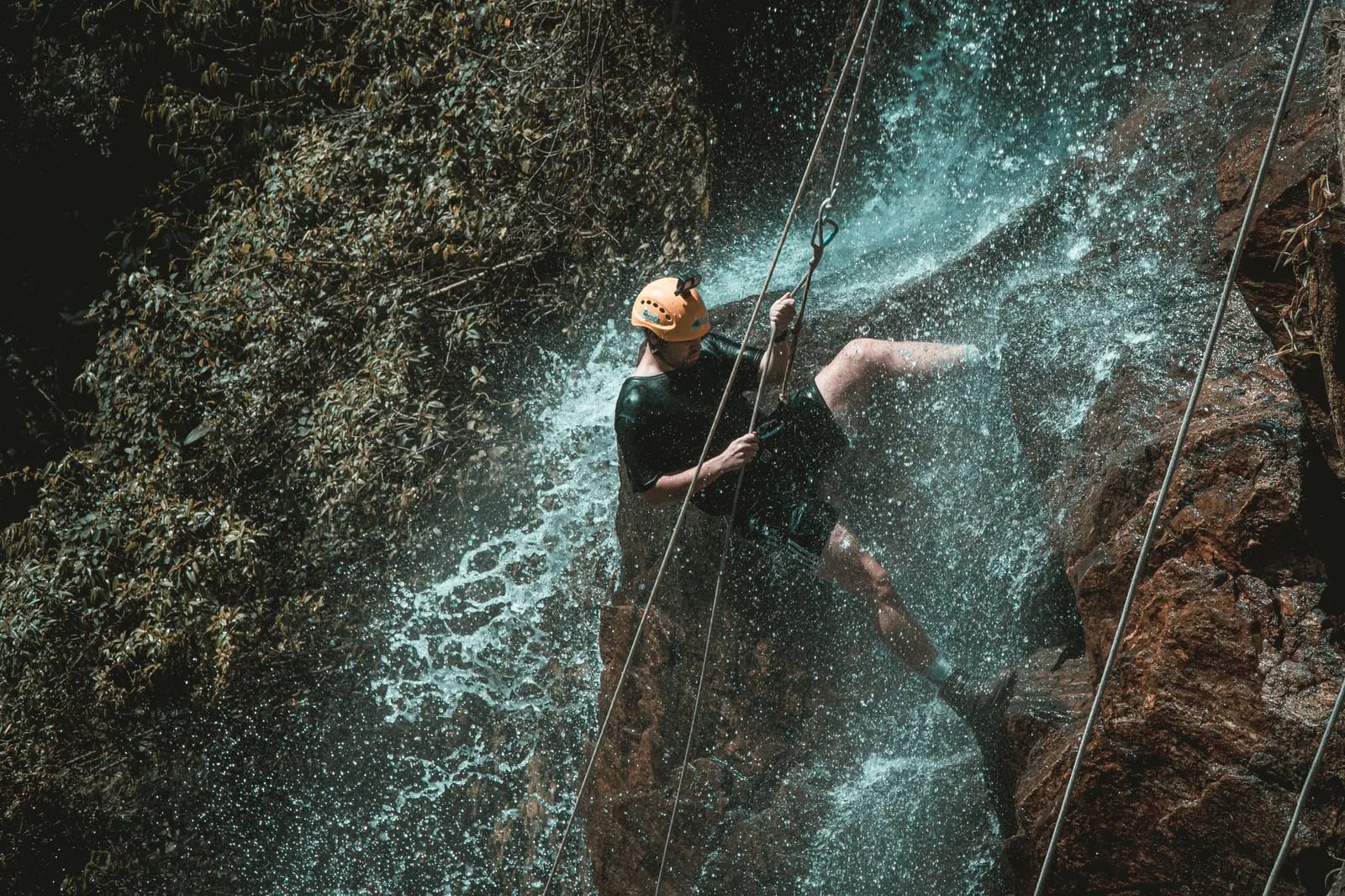 Canyoneur casqué descendant en rappel le long d'une cascade, cordes tendues sur la roche