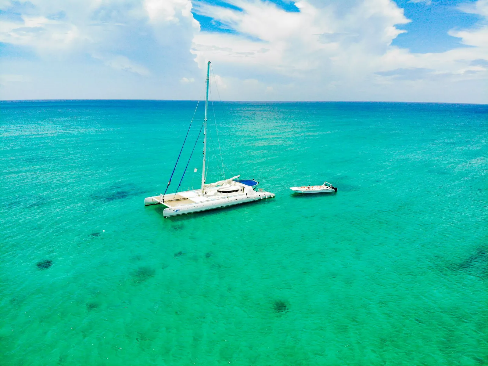 Catamaran à l'ancre sur un lagon turquoise, avec une annexe à côté, vue aérienne