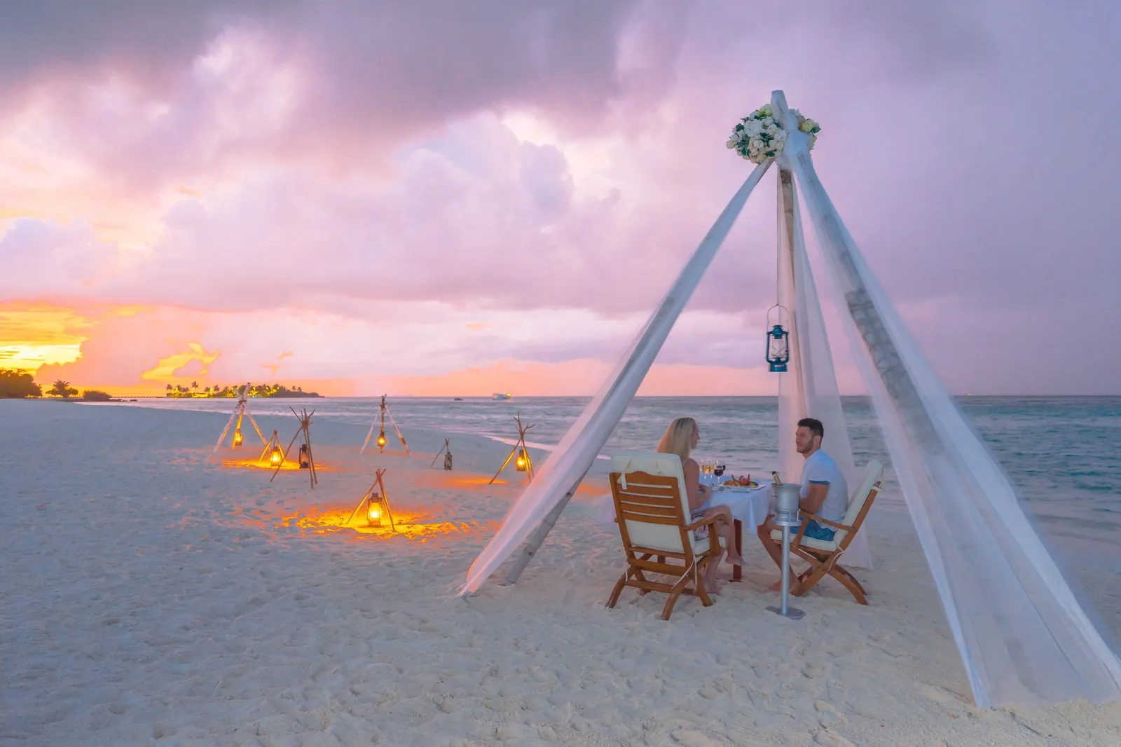Dîner pour deux sur la plage au coucher du soleil, avec lanternes et voilage