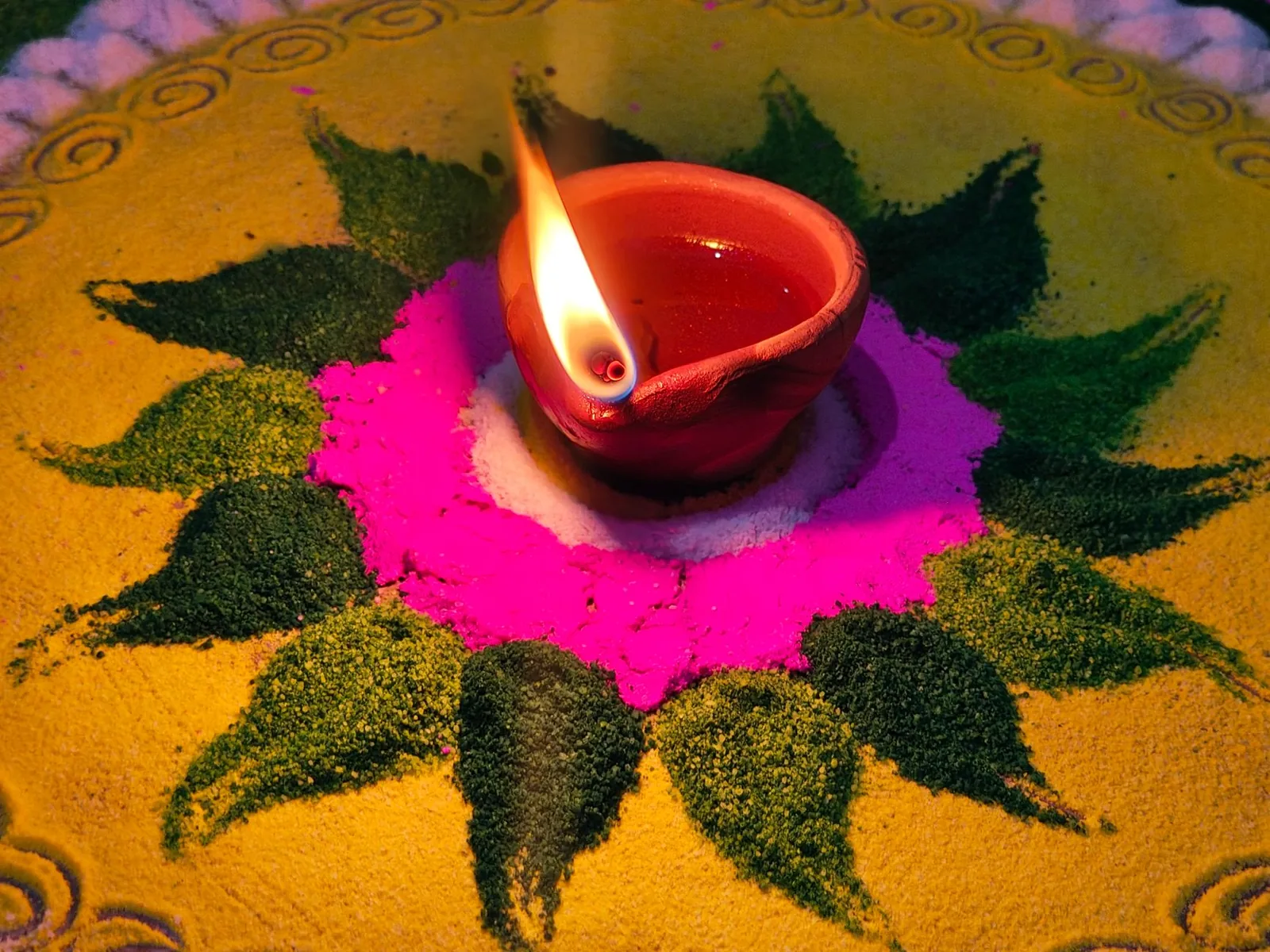 Diya allumée au centre d'un rangoli de poudres colorées, décoration traditionnelle de Divali