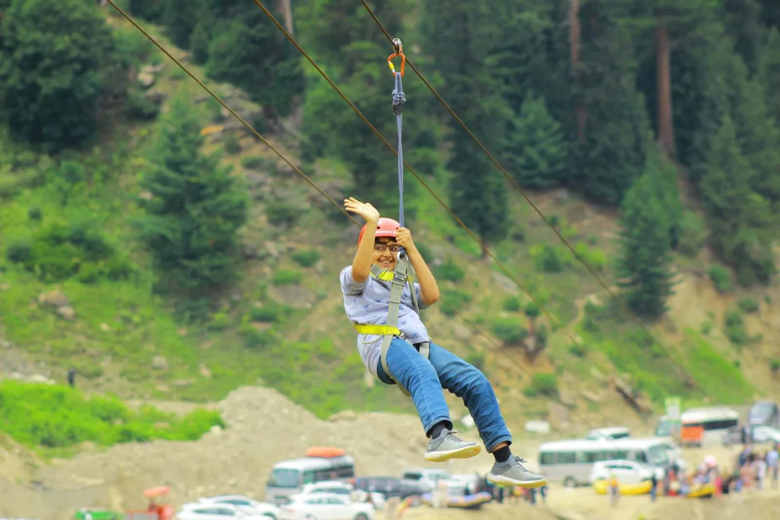 Enfant harnaché descendant une tyrolienne au-dessus d'une vallée boisée dans un parc aventure