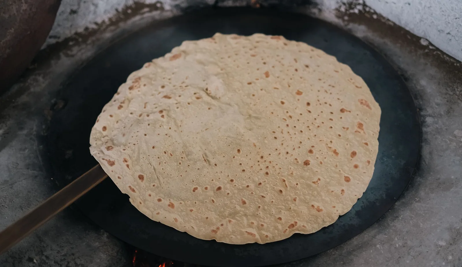 Galette fine en cuisson sur une grande plaque ronde en fonte, la méthode du dholl puri mauricien