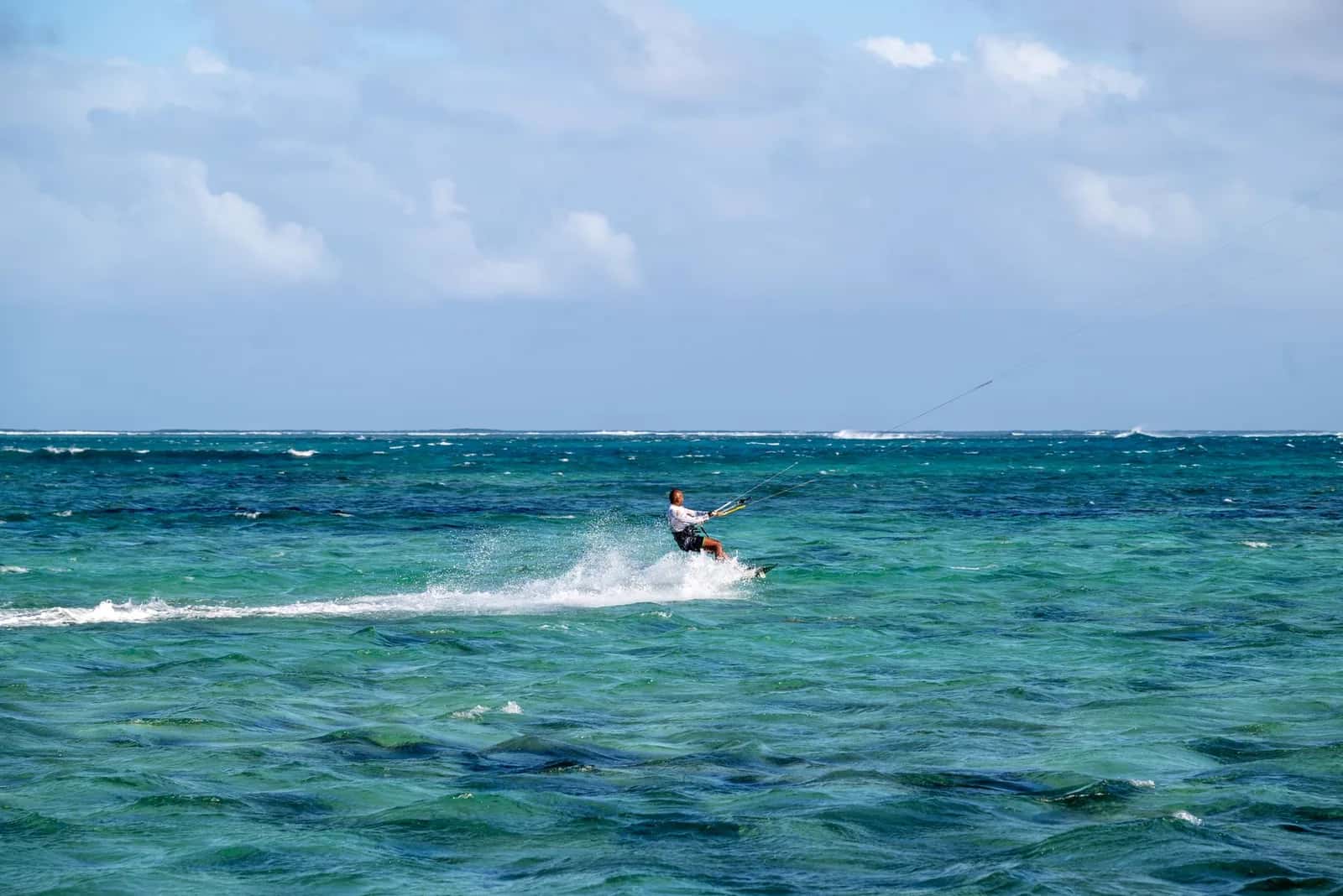 Kitesurfeur lancé dans un lagon turquoise agité par l'alizé, barrière de corail au fond, sur la côte de l'île Maurice