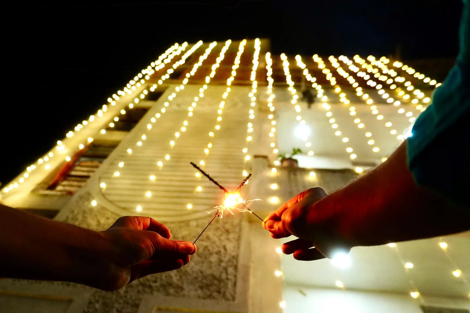 Façade couverte de guirlandes lumineuses la nuit, avec des cierges magiques allumés, pour Divali