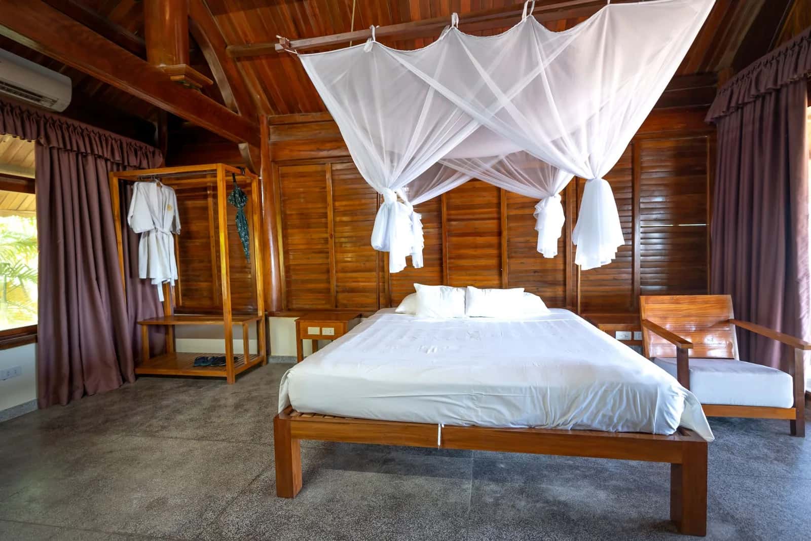 Lit à baldaquin équipé d'une moustiquaire dans un bungalow en bois tropical, avec climatisation murale