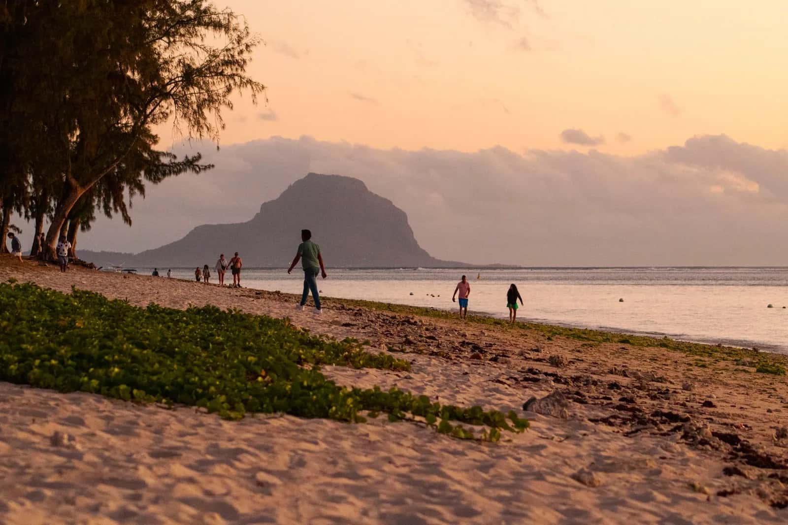 Promeneurs sur la plage de Flic en Flac à l'île Maurice au coucher du soleil, avec le Morne Brabant en arrière-plan