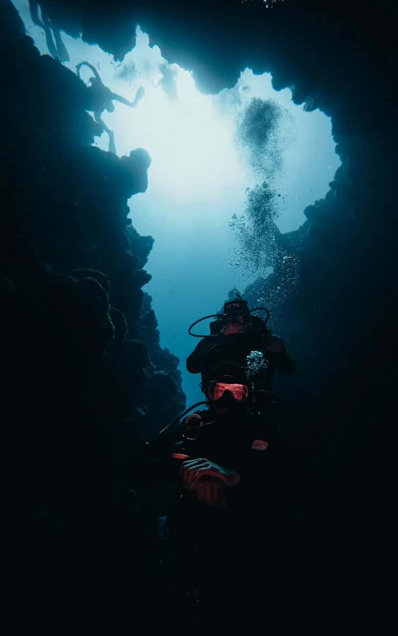 Deux plongeurs remontant dans une grotte sous-marine éclairée par le haut, comme à la Cathédrale au large de Flic en Flac
