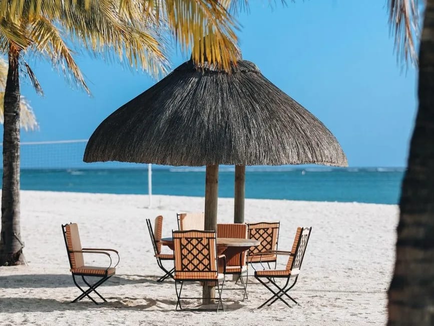 Table et chaises sous un parasol de chaume sur la plage d'un resort, face au lagon