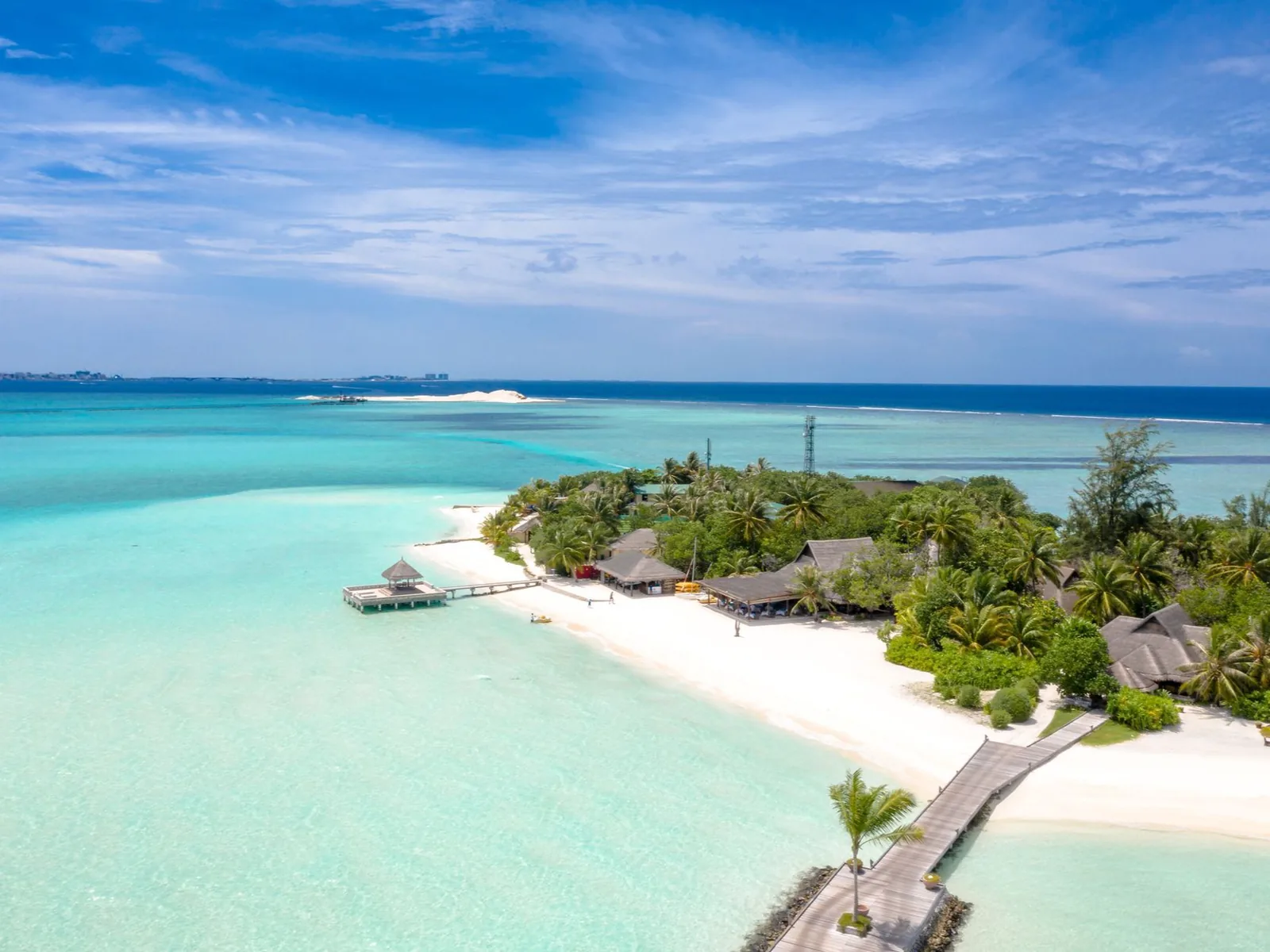 Resort tropical au bord d'un lagon turquoise calme, plage de sable blanc et ponton en bois