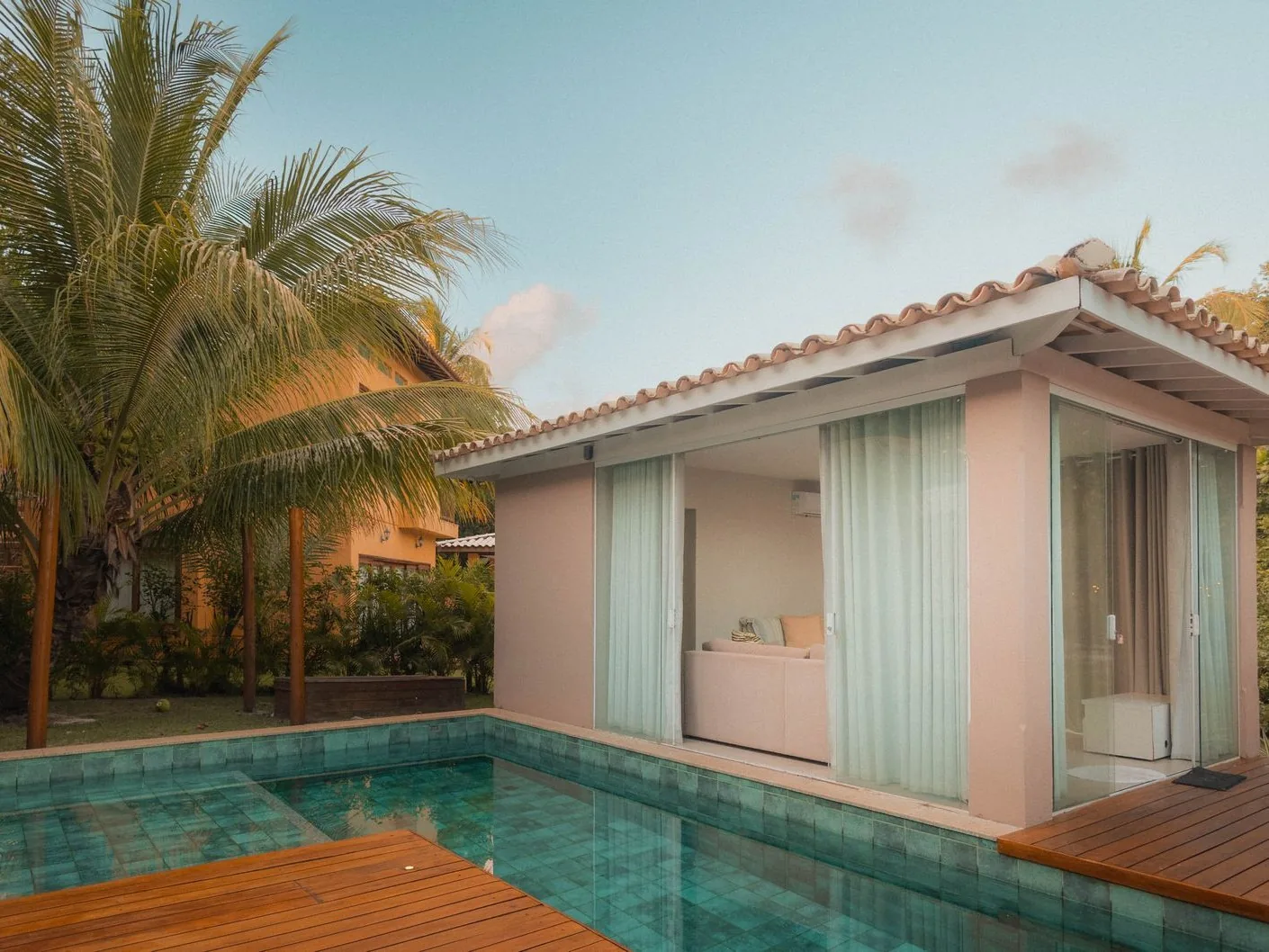 Piscine privée au carrelage turquoise, terrasse en bois et cocotiers dans un jardin tropical